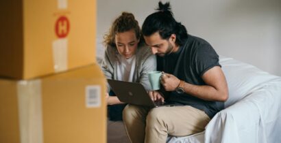 Couple surrounded by boxes checks laptop details on moving day.