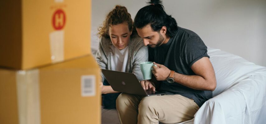 Couple surrounded by boxes checks laptop details on moving day.