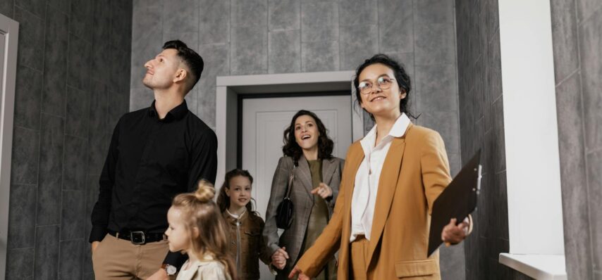 Happy family exploring a new home with a professional real estate agent guiding the tour. Dwellopolis.com