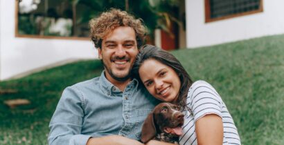 A joyful couple sitting on grass with their dog, enjoying a sunny day outdoors.