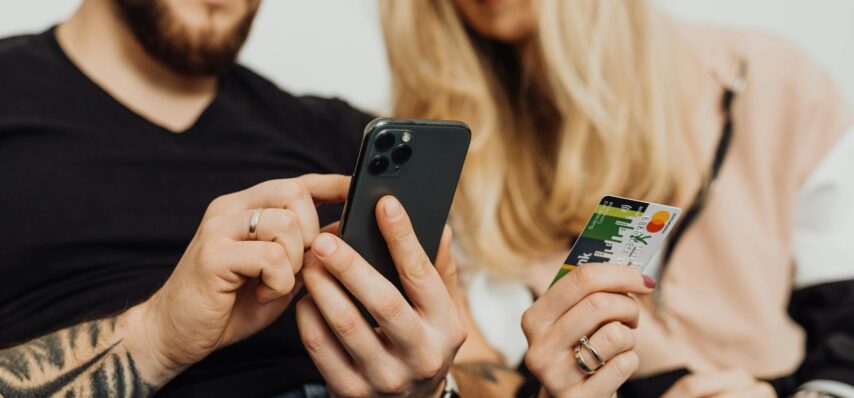 A couple using a smartphone and credit card for online shopping indoors.